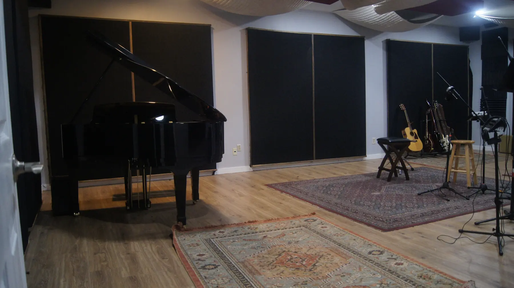 Wide view of Studio A’s live room, with the baby grand piano, hardwood floors, acoustic treatment, and space for musicians